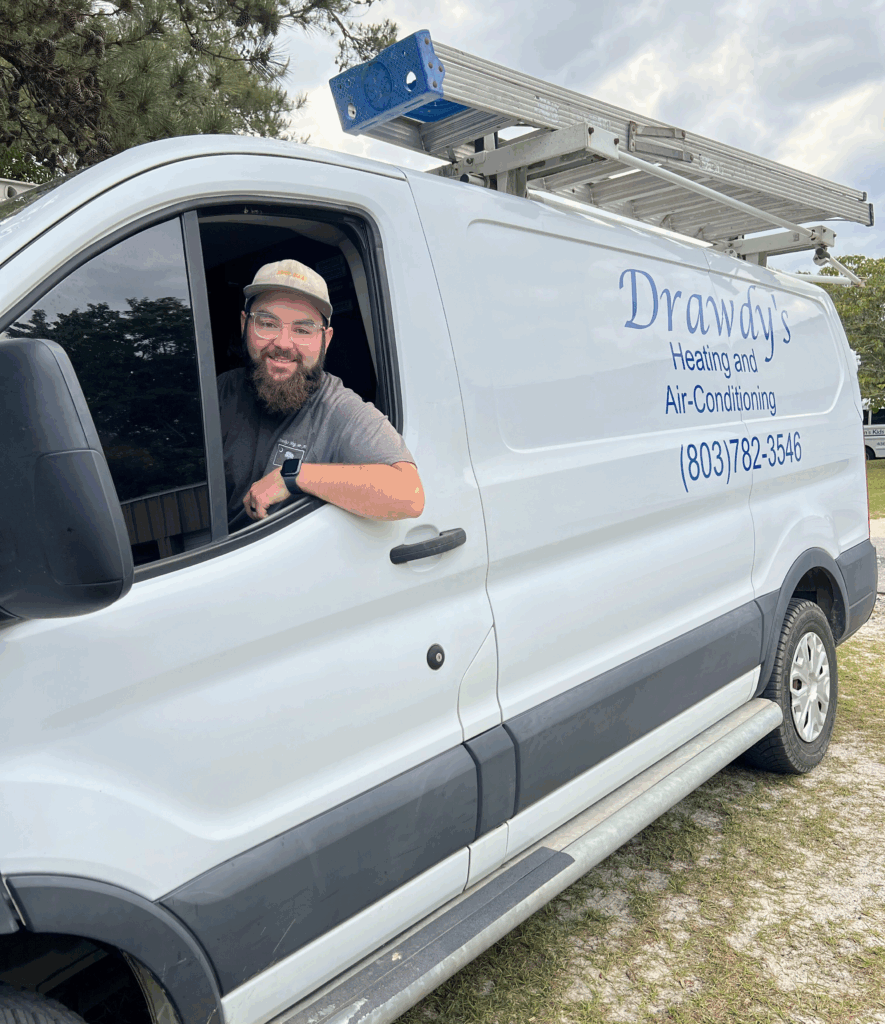 A man smiles from the window of a Drawdys Heating and Air-Conditioning van with a ladder on top.