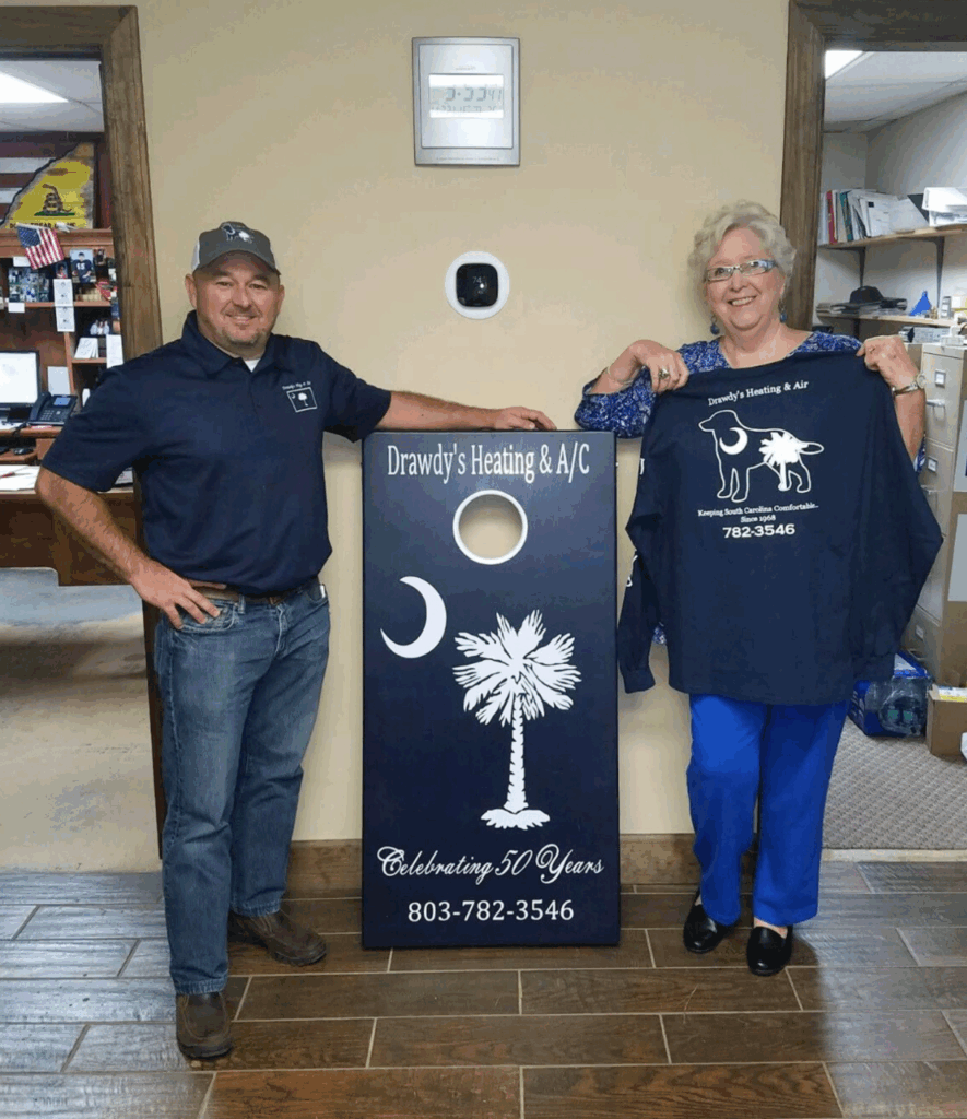 Two people pose with a custom cornhole board for Drawdy’s Heating & A/C’s 50th anniversary.